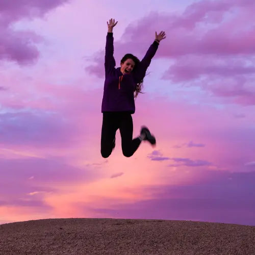 Joyful person jumping with arms raised in a purple sky during the holiday season.