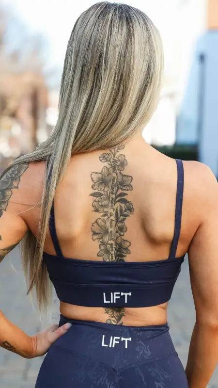 A floral spine tattoo between shoulder blades on a person wearing navy workout attire.