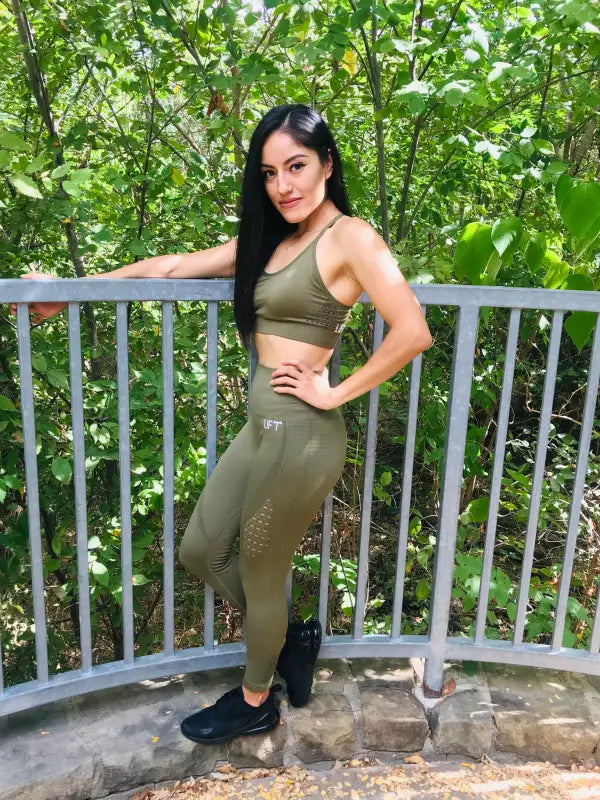 Woman in olive green athletic wear posing on a balcony.