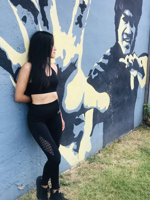 Woman in black athletic wear standing next to a wall mural.