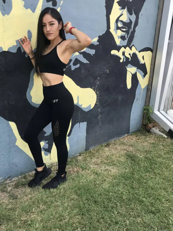 Woman in athletic wear posing in front of a mural.