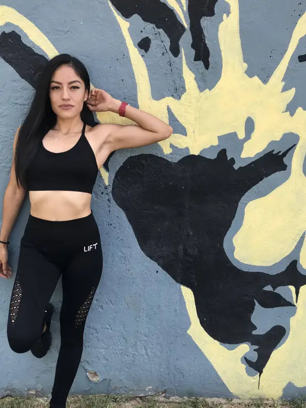 Woman in athletic wear posing against a painted wall.